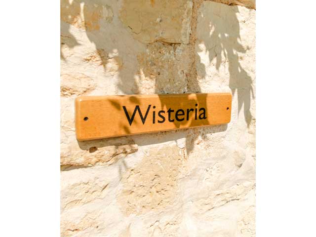 stone wall with a wooden sign reading 'Wisteria'