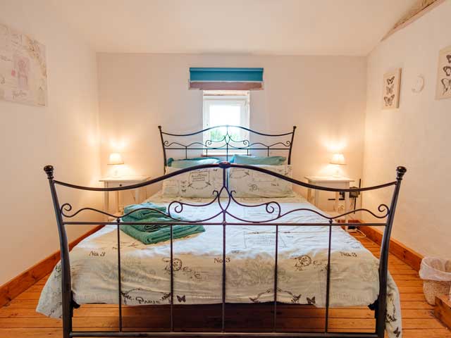 metal framed double bed in a white bedroom and window at the head. A pile of towels sit on the freshly made bed.