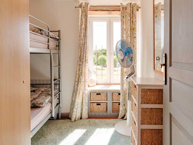 brightly lit bedroom with bunk beds and stand alone fan