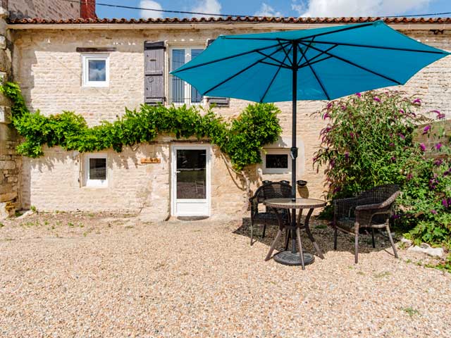 outdoor courtyard with gravel floor and bistro table and chairs and blue parasol.