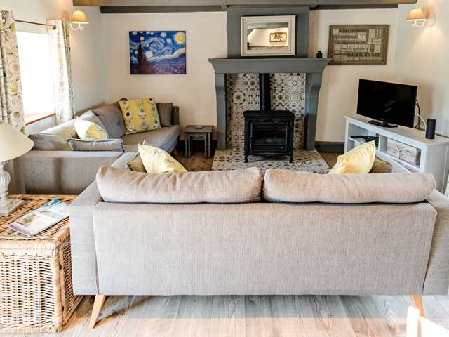 looking from the kitchen to the lounge area, across the top of the sofa, to see the woodburning stove and television