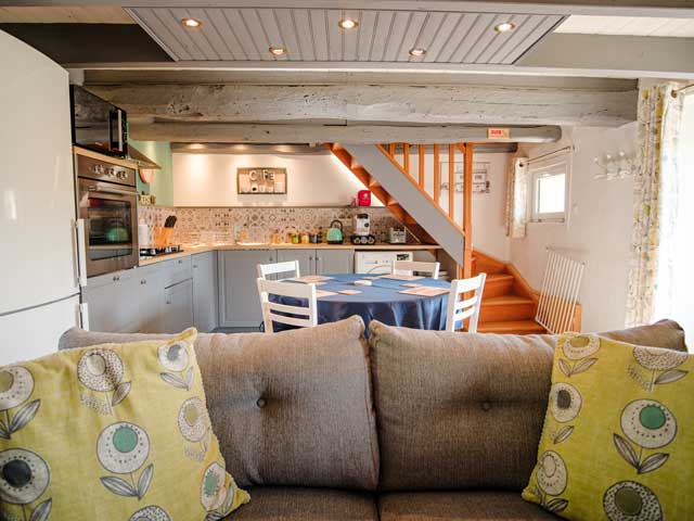 looking across the back of a dark grey sofa to see the kitchen and dining table and chairs