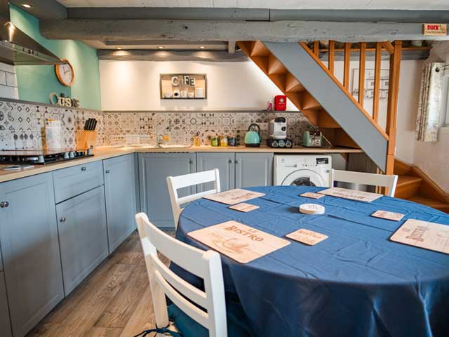 kitchen area with round dining table and chairs with stairs in the background leading up to the holiday accommodation