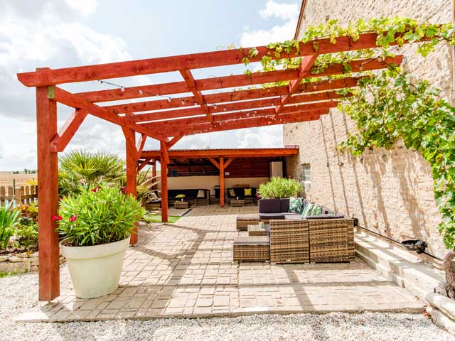wooden pergola structure in red wood leaning against the stone walls of the gites with summer seating underneath
