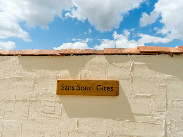 rendered exterior wall with tiles across the top and wooden sign reading 'Sans Souci Gites'