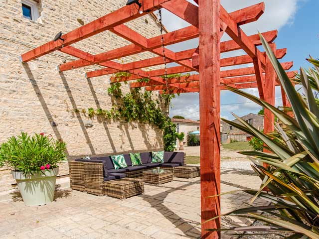 outdoor seating area on a ptio area with pergola above and large pot plants