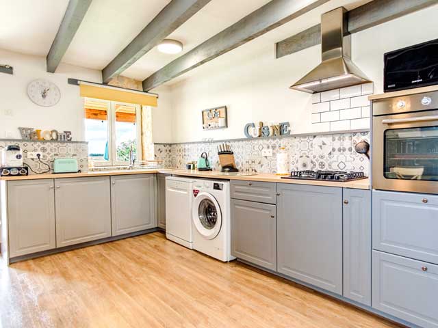 kitchen area with laminate floor, grey cupboards, white walls and oven, hob, washing machine, toaster, cofee maker