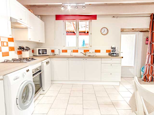 A very bright and airy looking kitchen with white tiles, cupboards, orange and red furninshings