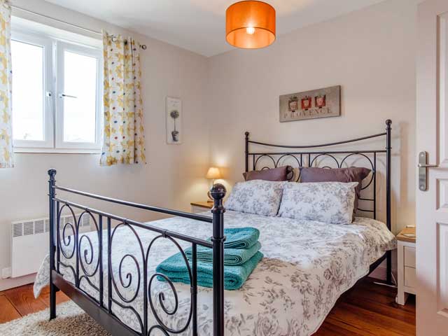 metal framed bed freshly made with towels on the bed. The room is light and airy and the window is open slightly