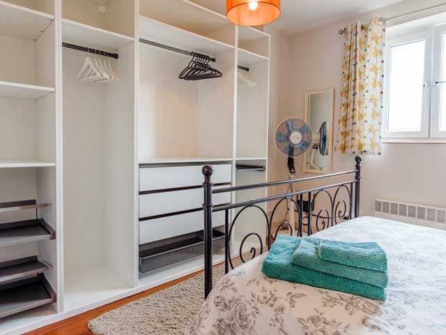 double bedroom with wardrobes and drawers, metal framed bed and a pile of clean towels on the bed