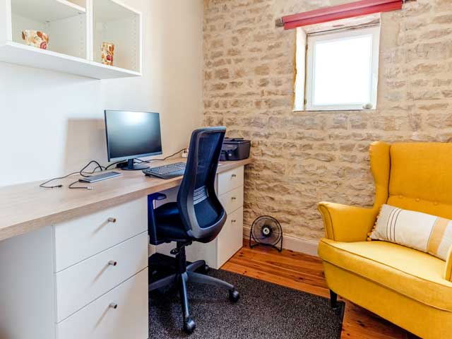 office area with desktop computer, wheely chair and comfortable yellow wing-backed chair