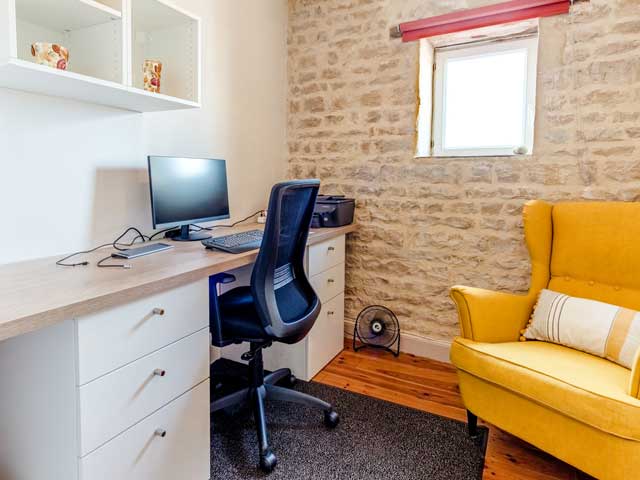 office area with desktop computer, wheely chair and comfortable yellow wing-backed chair