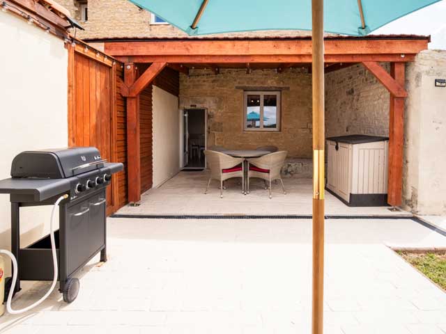 looking across the tiled section underneath the parasol to the dining table and chairs in the shaded area.