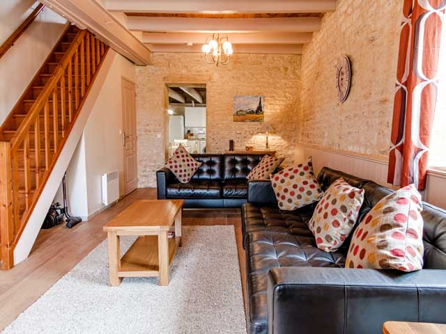 lounger area with two leather sofas and polka dot cushions, stone walls in the gite and a staircase leading up to the bedrooms