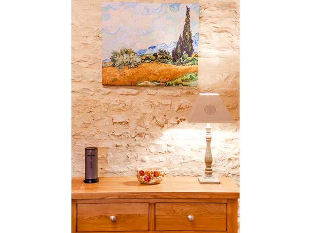 wooden furniture with a stone wall behind and a print of Van Gogh's Wheatfields picture hanging on the wall