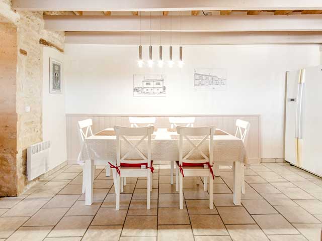 dining table with six chairs with a white wall behind and a large fridge to the right