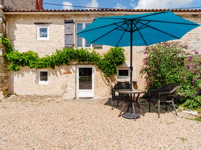 holiday accommodation with wisteria trailing across the front of the building and a large blue sun umbrella outside.