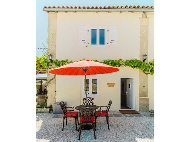 pretty cream coloured building with table and chairs outside on a gravel patio area with red parasol
