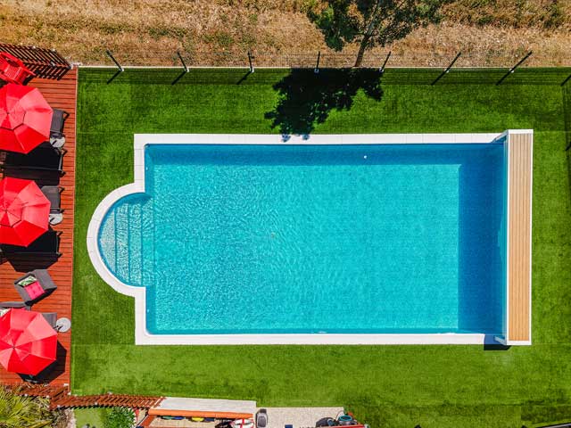 birds eye view of crystal blue swimming pool and a line of red parasol umbrellas